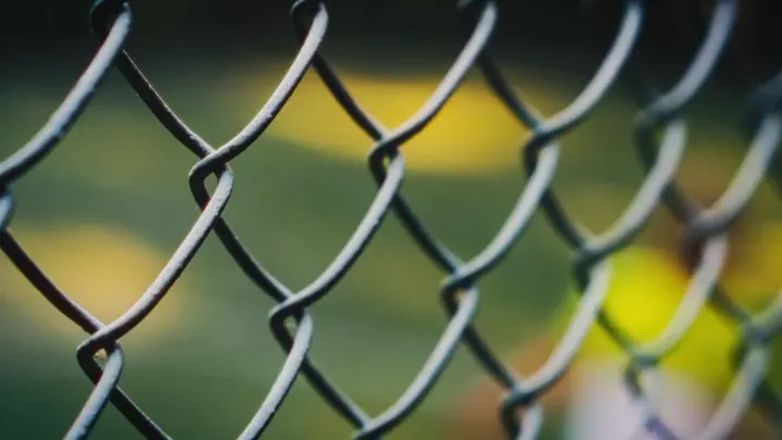 A wire fence in focus, colours behind it